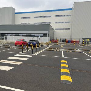 Brandsafe black and yellow flexible bollard delineators installed alongside parking stops and speed bumps in an Amazon vehicle parking and traffic management area.