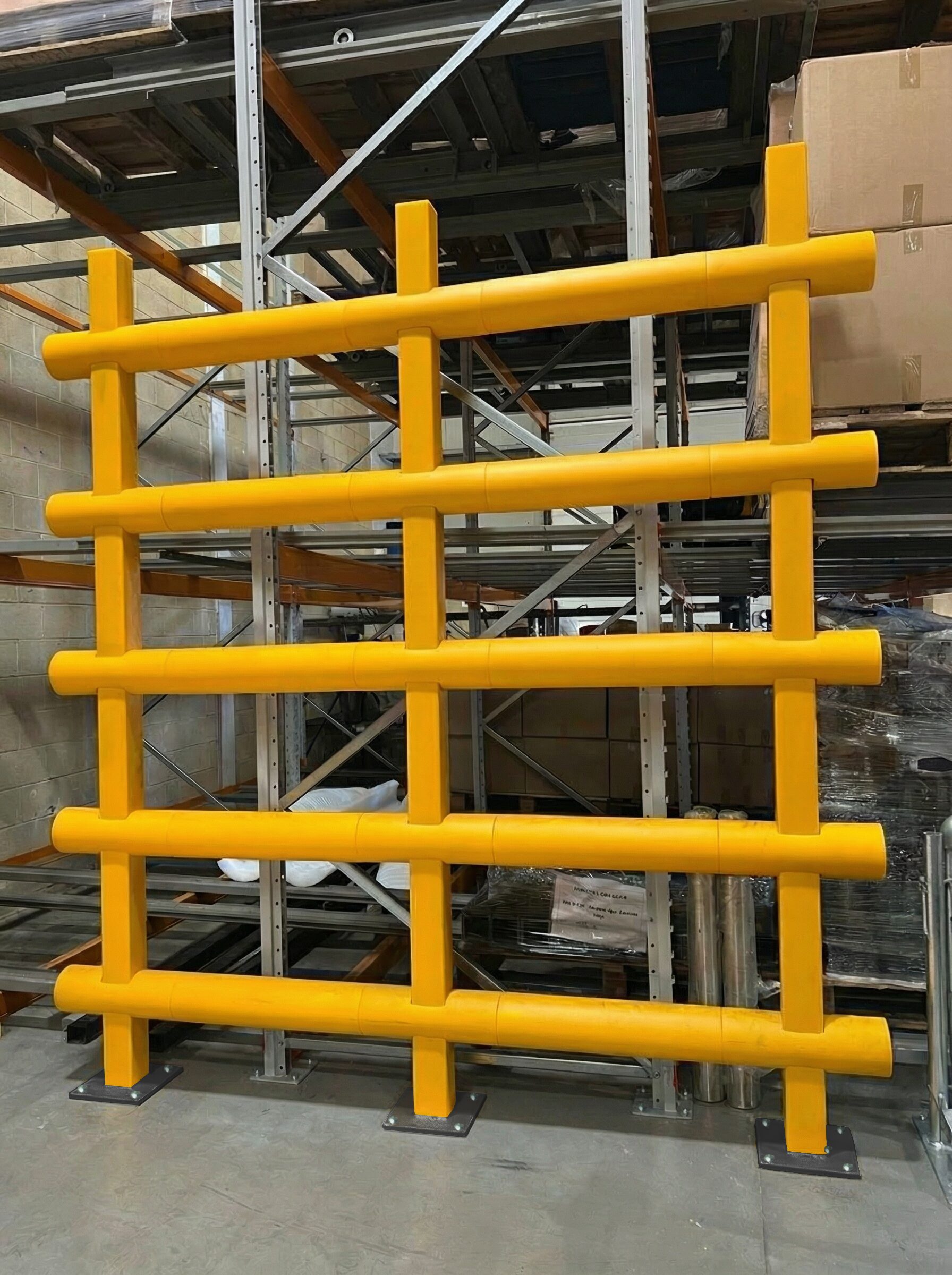 Yellow anti topple barrier protecting racking and loose stacked materials in a warehouse environment