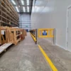 Long run of yellow polymer pedestrian barriers beginning at a safety gate beside marked floor lines