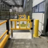 Two yellow pedestrian safety gates beside a loading bay door and marked warehouse crossing